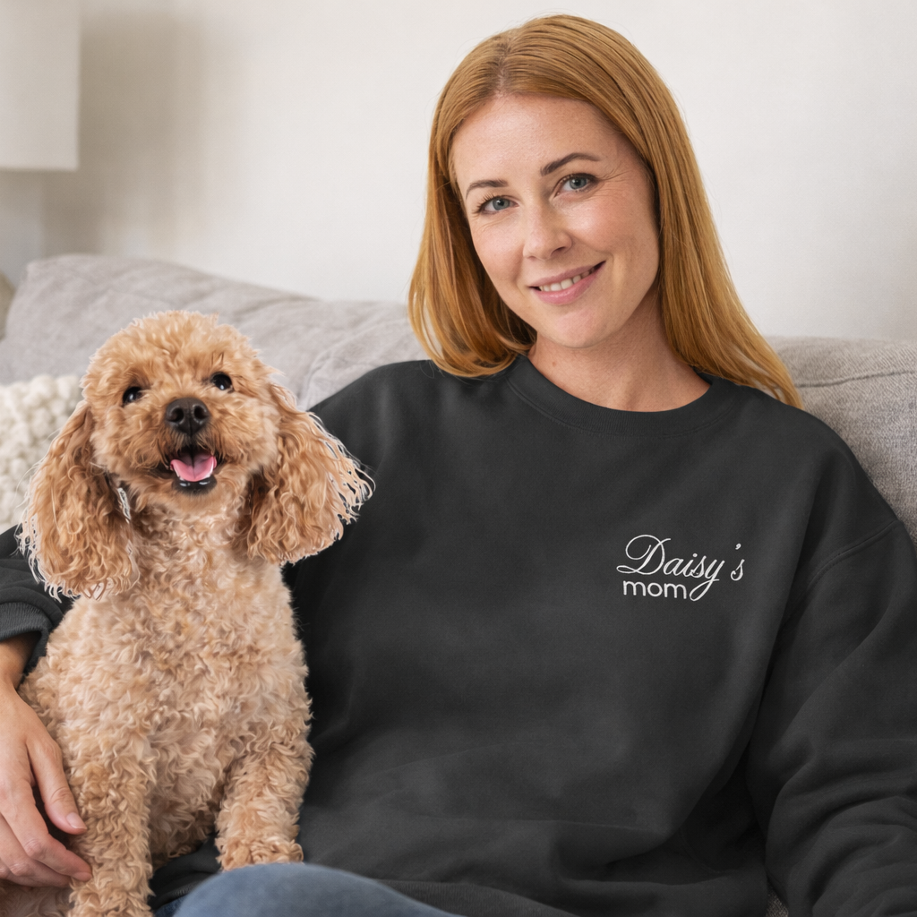 Woman wearing a black sweatshirt with 'Daisy's mom' text, sitting on a couch with a dog.